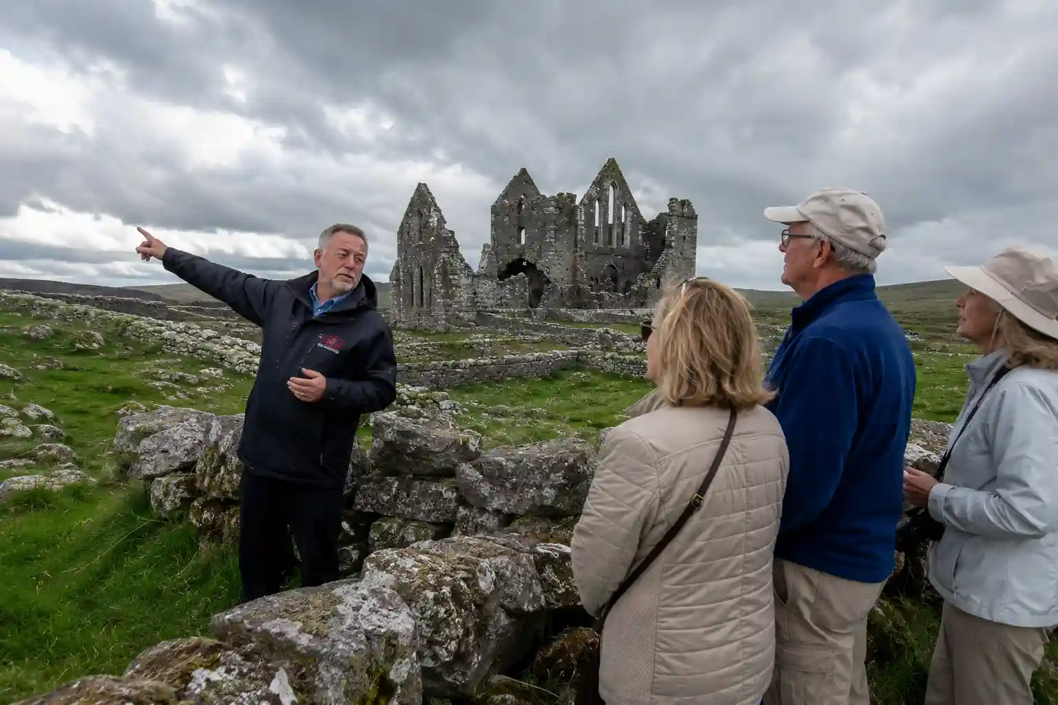 Irish driver-guide sharing local history with American visitors at ancient abbey ruin